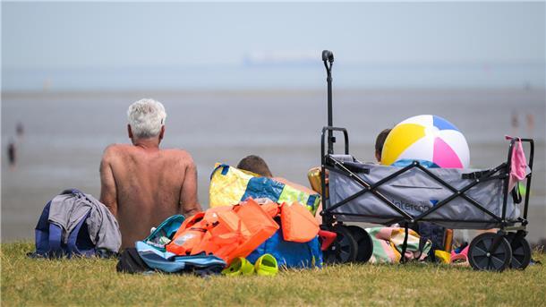 Ein Urlauber sitzt mit bloßem Oberkörper am Strand 