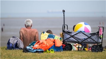 Ein Urlauber sitzt mit bloßem Oberkörper am Strand 