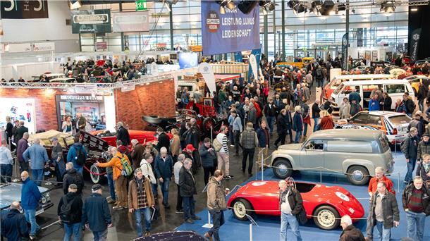 Viele Menschen in einer Halle zwischen Automobilen.
