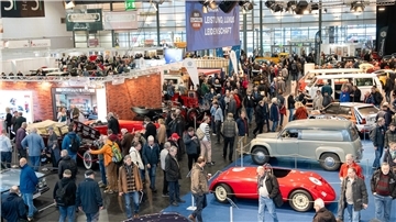 Viele Menschen in einer Halle zwischen Automobilen.