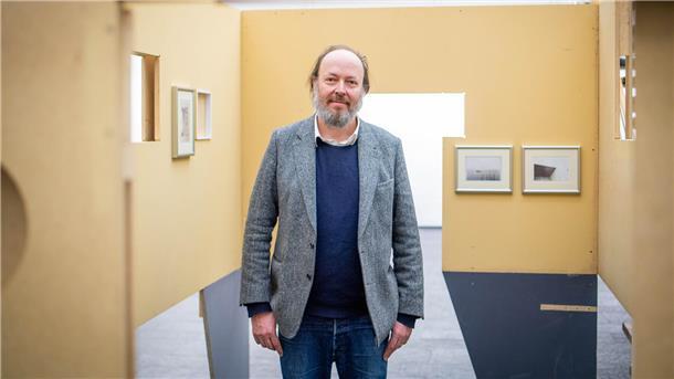 Ein Mann blickt in die Kamera, er steht in einer Ausstellung.