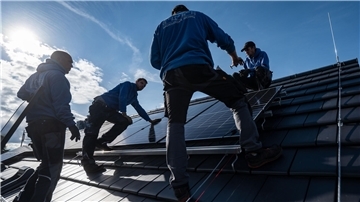 Männer installieren auf einem Hausdach Solarpaneele.