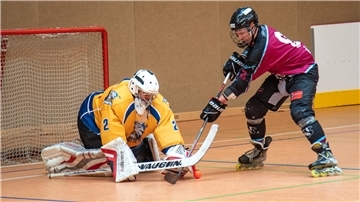 Ein Torhüter hält beim Inline-Skaterhockey den Ball eines Gegenspielers.