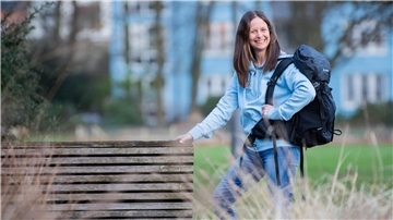 Eine Frau mit braunen Haaren und einer blauen Jacke steht mit einem Wanderrucksack im Grünen: Wanderliebhaberin Maria Luisa Kuzmic aus Bremerhaven.