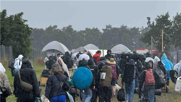 Stau, Regen und Chaos: Die Anreise zum Deichbrand 2024 wird zum Geduldsspiel! Menschen im Regen auf dem Weg zum Check-in des Deichbrand-Festivals.