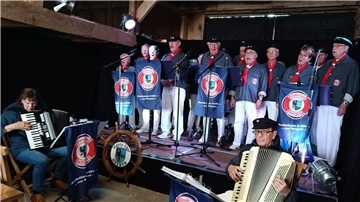 Mitglieder des Shanty-Chors Wremen stehen hinter Mikrofonen. 