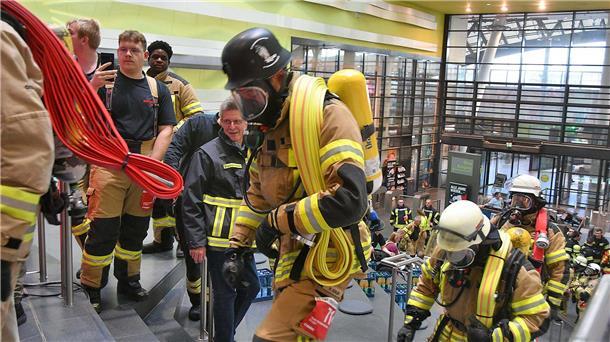Feuerwehrleute in voller Ausrüstung und unter Atemschutz rennen Stufen im Klimahaus empor