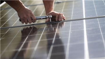 Mitarbeiter einer Firma montieren Photovoltaikmodule auf dem Dach eines Wohnhauses.