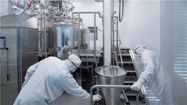Mitarbeiter eines Pharmaunternehmens arbeiten in einem Reinraum an einer Gelmischanlage.