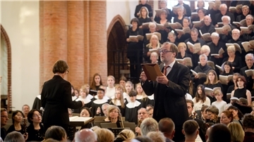 Dirigentin Eva Schad leitet Chor, Orchester und Solisten bei einer Aufführung in der Christuskirche, im Vordergrund ein Solist mit Notenmappe.
