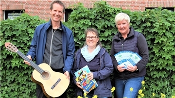 Musikschulleiter Pascal Gentner, Büchereileiterin Renate Schröter und Jugendpflegerin Martina Feldmann-Bienhoff werben vor einer grünen Hecke für die Veranstaltung "Little Motion" in Hagen