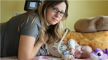 Eine Frau liegt mit krankem Baby auf einem Bett. 