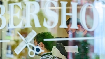 Ein Friseur schneidet einem Kunden im „Barbershop“ die Haare.