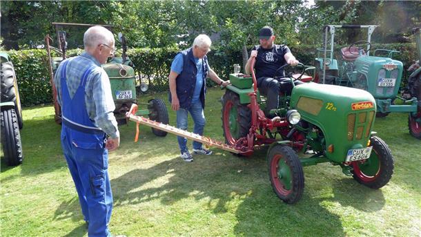 Drei Männer begutachten einen restaurierten grünen Holder-Traktor mit 12 PS auf einer Wiese. Im Hintergrund stehen weitere historische Traktoren verschiedener Marken.