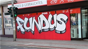 Nach einem Unfall ist das Schaufenster des Fundus mit Sperrholz verkleidet. Eine Graffiti-Aktion macht daraus einen farbenfrohen Blickfang.