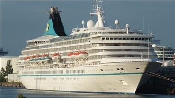 Das Kreuzfahrtschiff „Artania“ liegt im Hafen. Das weiße Schiff mit türkisfarbenen Details verfügt über mehrere Decks, auf denen Rettungsboote zu sehen sind. Der markante Schornstein trägt das Logo von Phoenix Reisen.