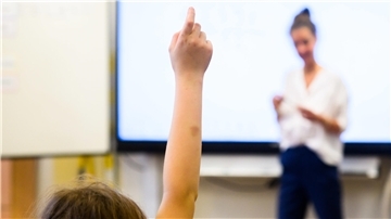 Ein Schüler meldet sich per Handzeichen in einem Klassenraum. 