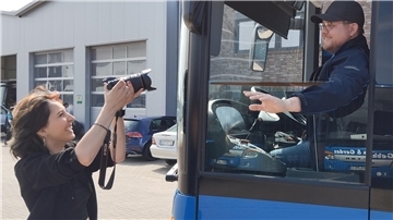 Eine Frau fotografiert einen Busfahrer. 