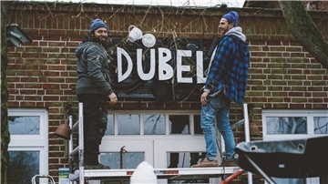 Fynn und Baldo stehen auf einem Gerüst und bauen das neue Logo vom Dübel, der Kliemannsland-Gastro, an.