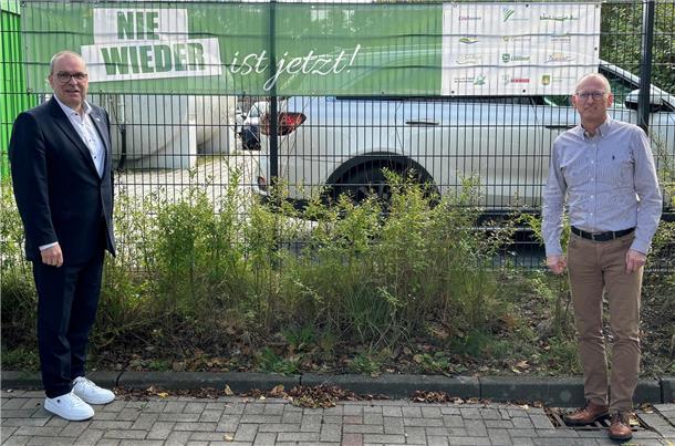 Zwei Männer stehen vor einem Banner, auf dem „Nie wieder ist jetzt!" zu lesen ist. 