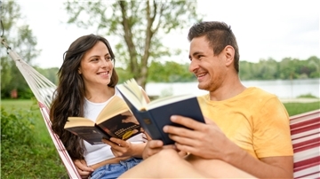  Ein junges Paar liest in einer Hängematte in ihren Büchern.
