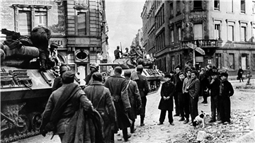 Ob die US-Soldaten damals wohl als Befreier oder Besatzer begriffen wurden? Eine Gruppe Jugendlicher steht am Straßenrand und beobachtet den Einmarsch gegen Ende des Zweiten Weltkriegs.