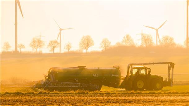 Mit einem Traktor wird bei Sonnenaufgang ein Feld in der Region Hannover mit Gülle gedüngt.