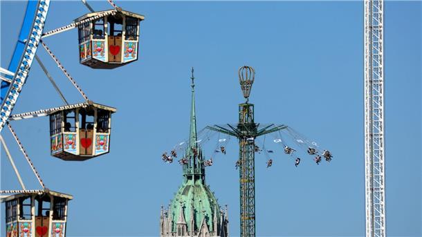 Oktoberfestbesucher fahren im Kettenkarussell zwischen Riesenrad und Paulskirche.