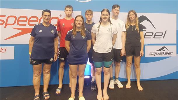 Schwimmerinnen und ihre Trainerinnen lächeln in die Kamera.