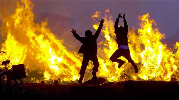 Zwei Menschen springen vor einem Osterfeuer in die Luft.