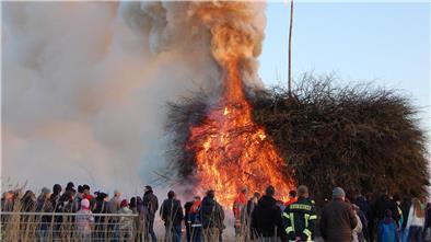 Menschen stehen um ein brennendes Osterfeuer herum.