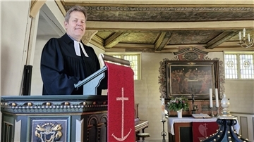 Ein Pastor im Talar steht in der Kanzel einer kleinen Kirche.