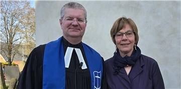 Ein Mann, der evangelischer Pfarrer ist, und eine Seemannsdiakonin stehen vor einer Kirche.