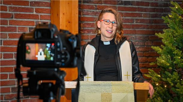 Pastorin an einem Pult, Videokamera im Vordergrund.