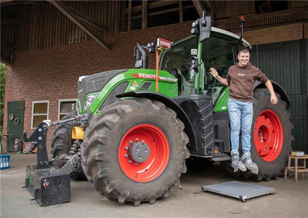 Ein junger Mann mit braunem Sweatshirt und blauer Jeans springt von einem Traktor.