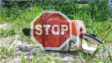 Eine Motorsäge liegt auf einem steinigen Untergrund mit hohem Gras im Hintergrund. Darüber ist ein rotes Stoppschild mit der Aufschrift 'STOP' transparent eingeblendet.