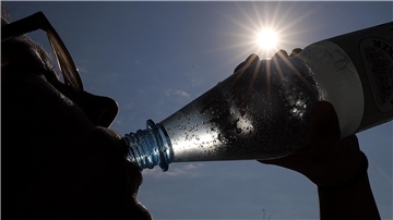 Eine Frau trinkt in der Sonne Mineralwasser.
