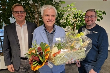Gruppenfoto Drei Männer der in der Mitte hat einen Blumenstrauß