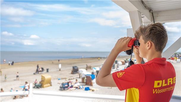 DLRG sucht Rettungsschwimmer für Badesaison Peter von der DLRG-Wasserrettung steht auf einem Turm und beaufsichtigt mit einem Fernglas den Badestrand von Dangast.