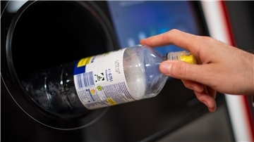 Ein Mann steckt eine Pfandflasche in einen Pfandflaschenautomaten in einem Supermarkt. 