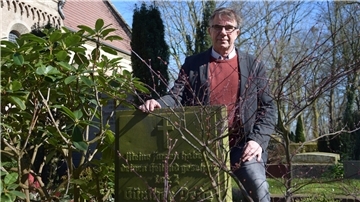 Der Pfarrer Dietmar Reumann-Claßen steht hinter dem Grab von Günther Dede auf dem Kirchenfriedhof in Blexen. 