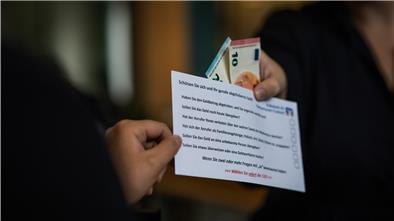 Eine Person überreicht Geld in einem Briefumschlag an eine weitere Person.