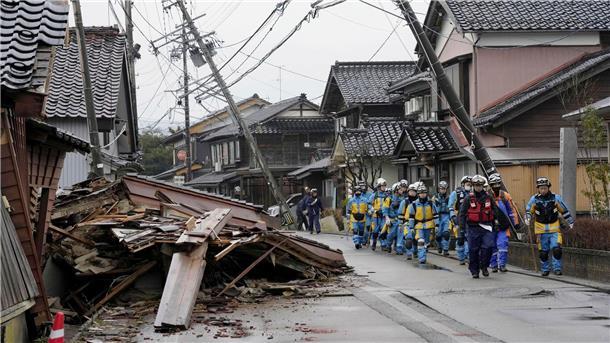 Japan untersucht Flugzeugkollision - Weitere Bebenopfer Polizisten gehen an eingestürzten Häusern in Suzu vorbei.