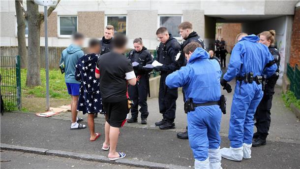 Polizeieinsatz in Wohnkomplex: Gegenstände sichergestellt Polizisten, zum Teil in Schutzkleidung, kontrollieren Anwohner vor einem Wohnkomplex.