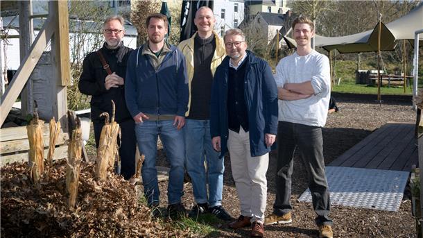 Fünf Männer stehen auf einem Gelände im Freien und blicken in die Kamera.