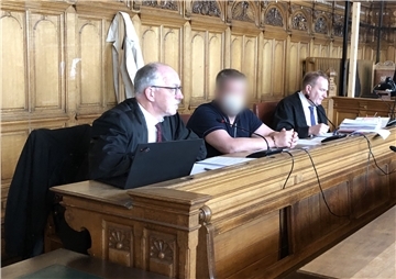 Drei Männer sitzen in einem Gerichtssaal. 
