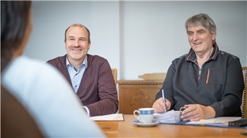 Ein Projektorganisator und ein Dozent sitzen an einem Tisch.