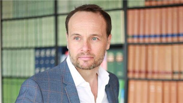 Rechtsanwalt Wolfgang Wittmann steht vor einem Bücherregal.