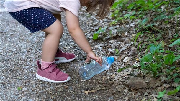 Ein Kind hebt Plastikflasche auf. Am 18. März ist Tag des Recyclings.