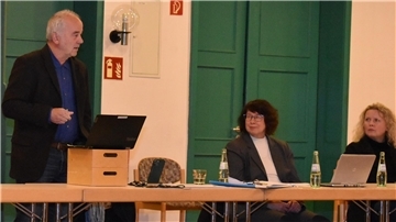 Ein Mann und zwei Frauen hinter Tischen 